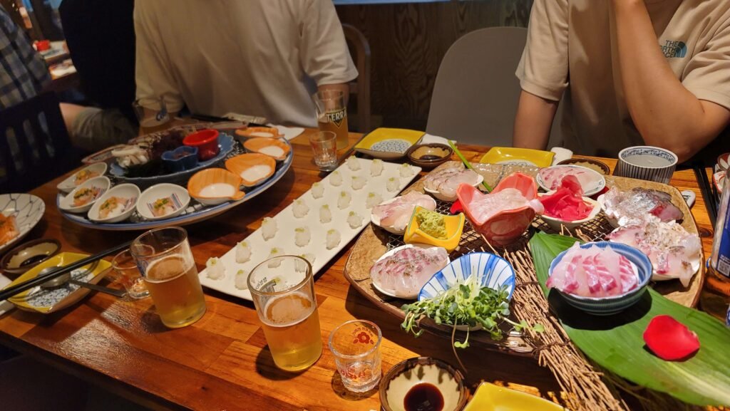 A spread of fresh Jeju Island sashimi, sushi, and seafood side dishes with beers, showcasing a local dining experience for Jeju Island travel.