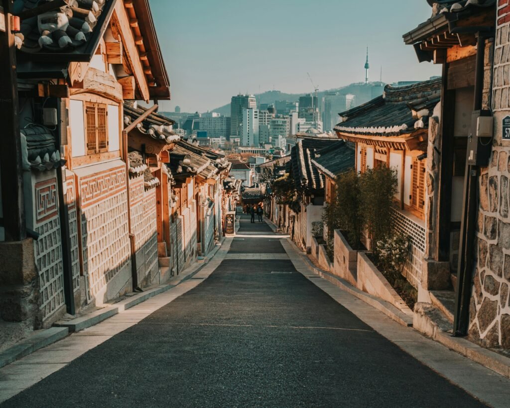 A wide, panoramic view of a traditional Korean Buddhist temple complex built in Hanok architecture, nestled peacefully in a green mountain valley under a partly cloudy sky