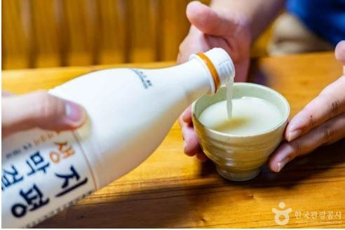 A foreign tourist smiling while stirring rice and yeast to brew Makgeolli, a popular Korean traditional food experience